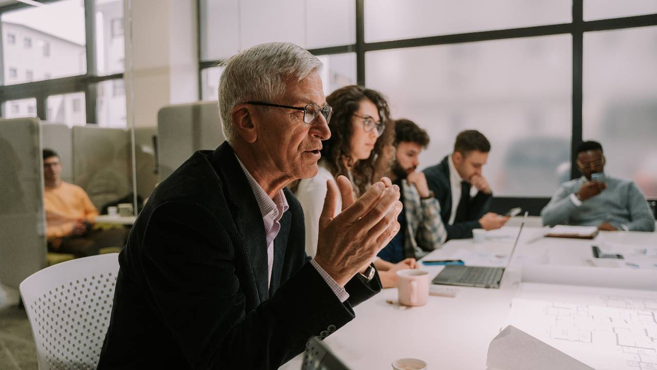 A senior man talking to his colleague at the other side of the table